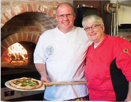 Owners Dutch and Rebecca Van Oostendorp man and woman standing in front of a pizza oven